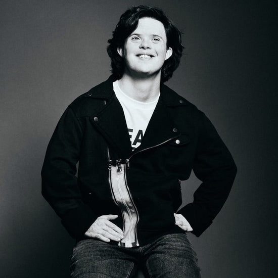 A black and white photo of a young white man smiling with full black hair in a black motocross jacket with a gray ZipperBuddy Magzip