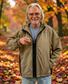 Smiling man with gray hair in a tan jacket zipped with a ZipperBuddy, standing among autumn leaves